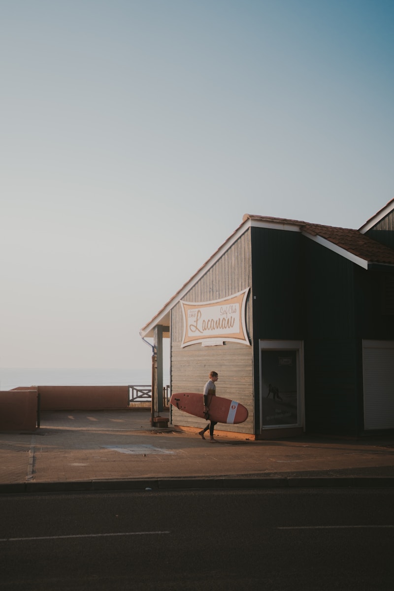 A person walking towards a building with a surfboard in front of it